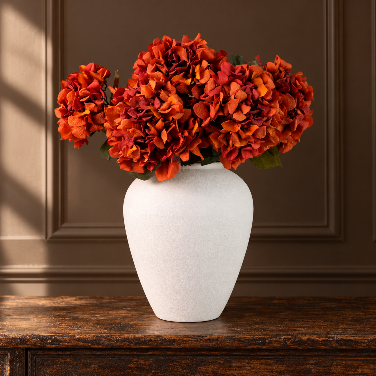 Burnt orange real touch garden hydrangea stems arranged in a white vase on a dark wooden console