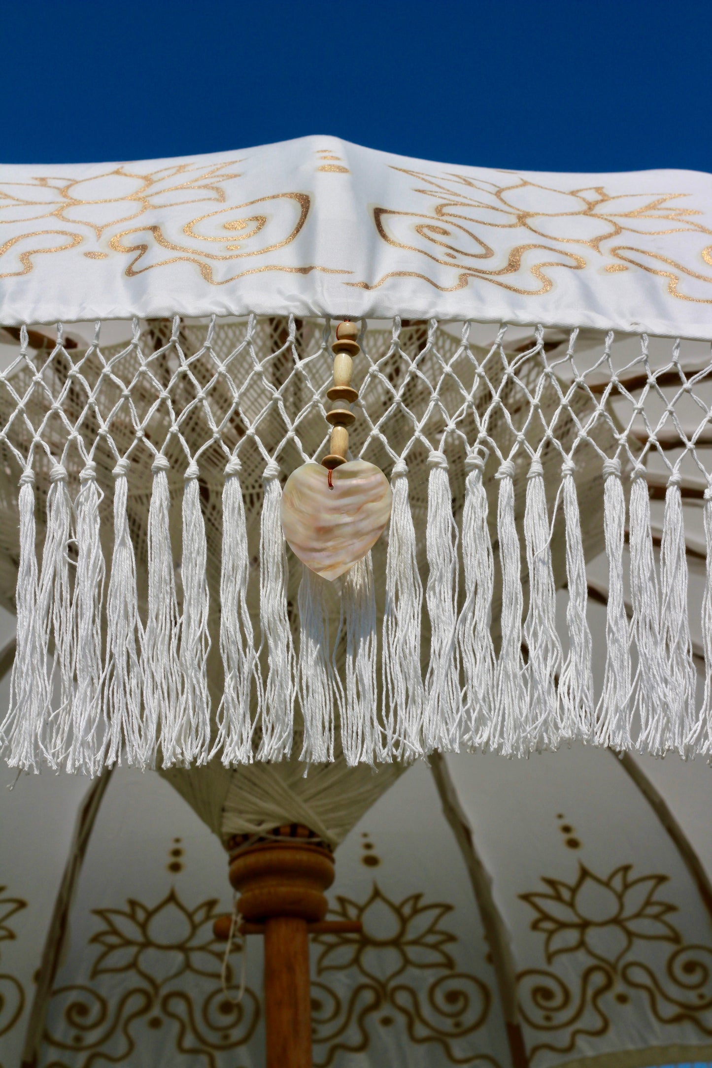 Decorative outdoor parasol in white with gold floral detailing and a fringed edge