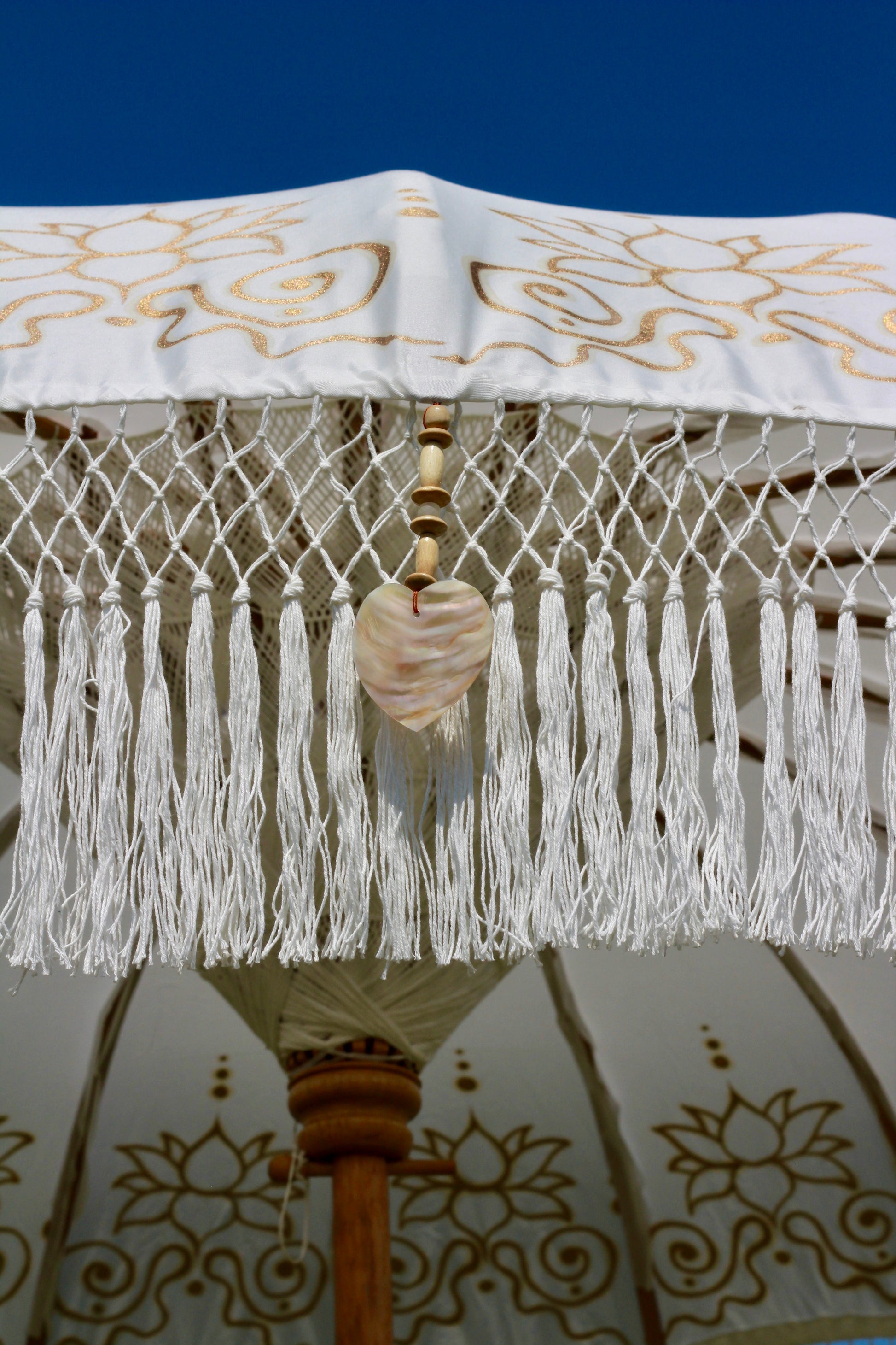Decorative outdoor parasol in white with gold floral detailing and a fringed edge