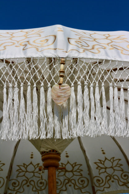 Decorative outdoor parasol in white with gold floral detailing and a fringed edge