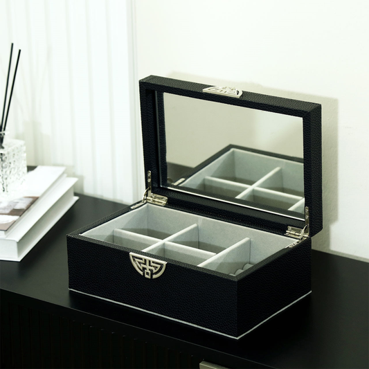 Open jewellery storage box with mirror and multiple interior sections on a black cabinet
