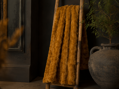 Whiskey brown faux fur ruffle throw styled across a sofa in a warm neutral interior.